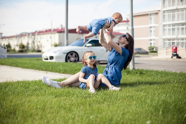 Young mother with daughters are sitting on the grass.