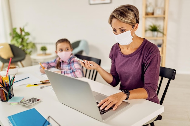 Young mother with face mask working on laptop at home due to coronavirus epidemic