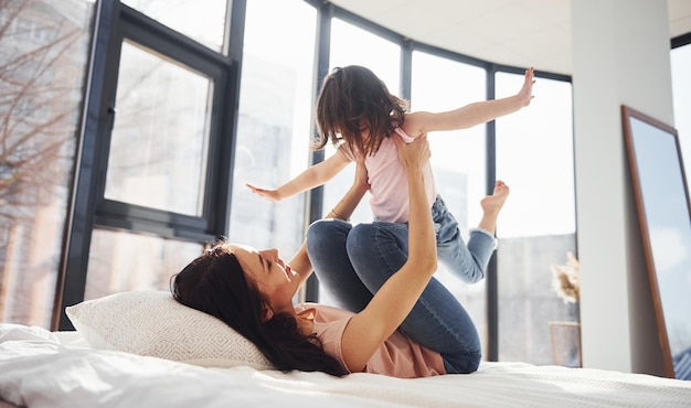 Young mother with her daughter have fun at weekend time together on bed