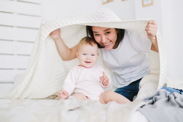 Young mother with her daughter play hide and seek in the bedroom