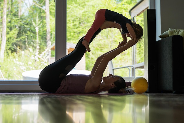 Young mother working out and doing yoga at home with her little toddler daughter.