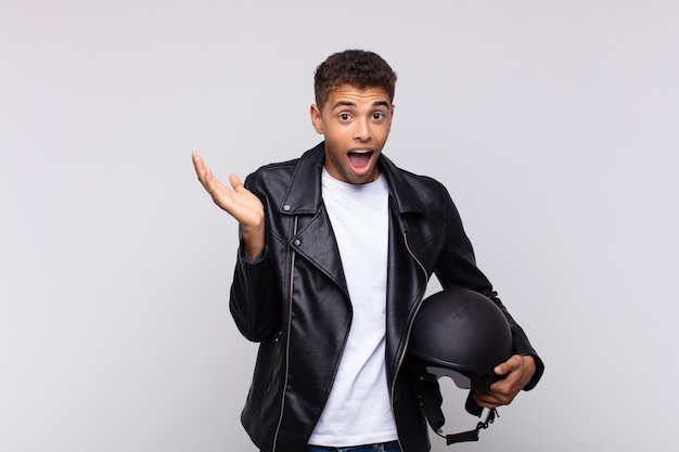 Young motorbike rider feeling happy, excited, surprised or shocked, smiling and astonished at something unbelievable