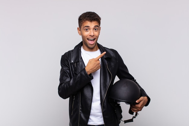 Young motorbike rider looking excited and surprised pointing to the side and upwards to copy space