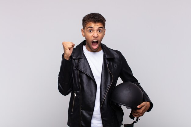 Young motorbike rider shouting aggressively with an angry expression or with fists clenched celebrating success