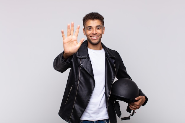 Young motorbike rider smiling and looking friendly, showing number five or fifth with hand forward, counting down