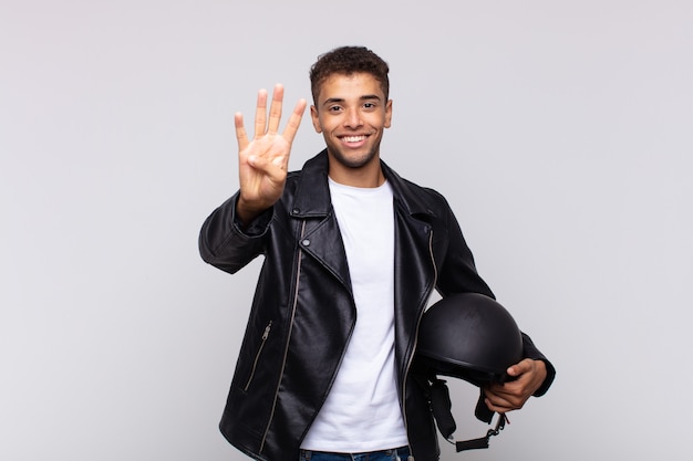 Young motorbike rider smiling and looking friendly, showing number four or fourth with hand forward, counting down