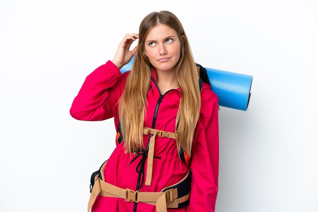 Young mountaineer girl with a big backpack over isolated white background having doubts and with confuse face expression