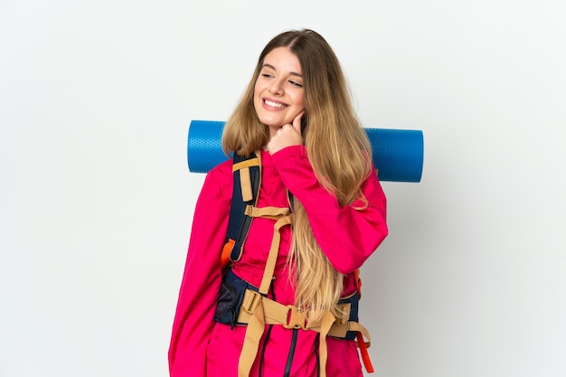 Young mountaineer woman with a big backpack over isolated space looking to the side and smiling