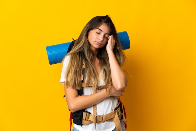 Young mountaineer woman with a big backpack on yellow with headache