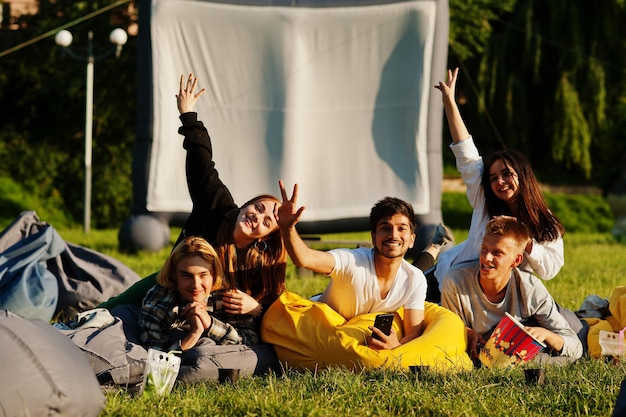 Young multi ethnic group of people watching movie at poof in open air cinema.