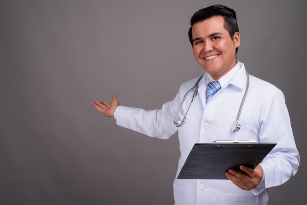 Young multi-ethnic man doctor against gray wall