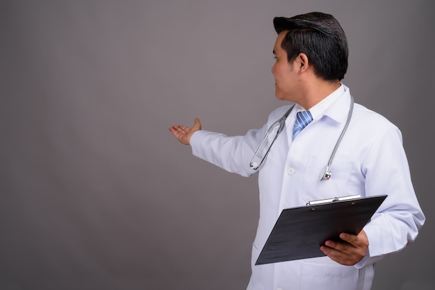 Young multi-ethnic man doctor against gray wall