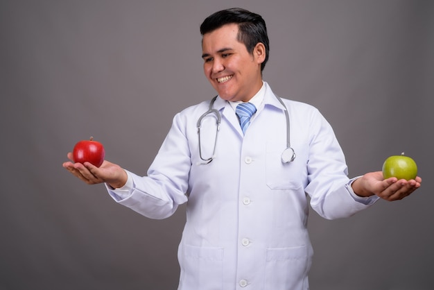 Young multi-ethnic man doctor against gray wall