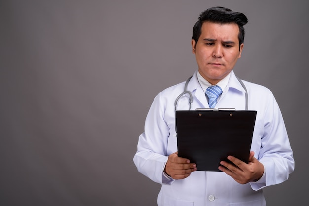 Young multi-ethnic man doctor against gray wall