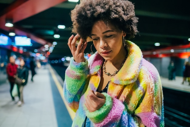 Young multiethnic woman underground using phone listening vocal message