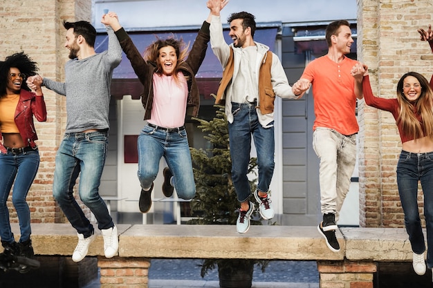 Young multiracial friends having fun jumping outdoor in the city - Focus on center man face