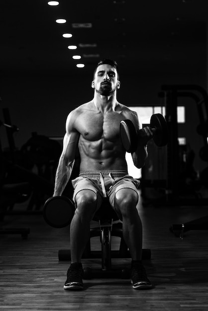 Young Muscular Man Doing Heavy Weight Exercise For Biceps With Dumbbells In Gym