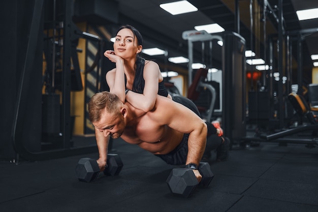 Young muscular man doing pushup exercise and holding girl joint training group lessons teambuilding romance