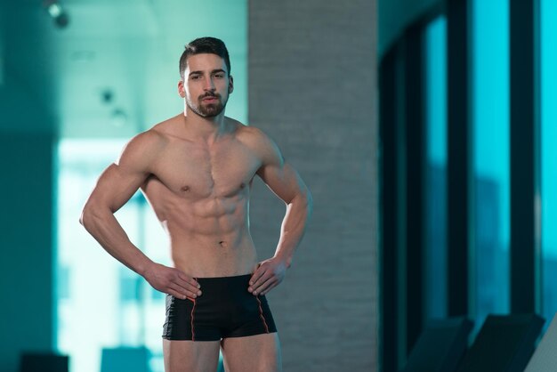 Young Muscular Man Flexing Muscles By Swimming Pool And Sun Loungers