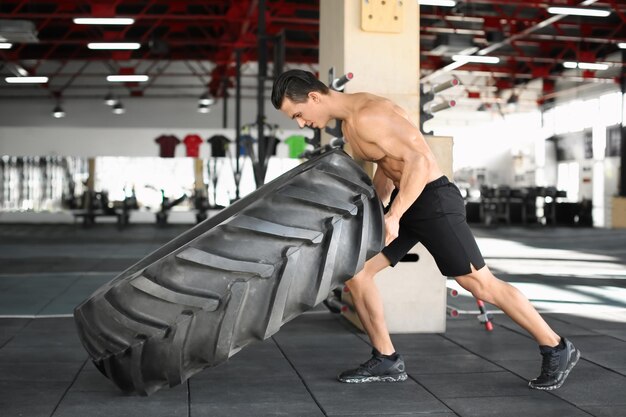 Young muscular man flipping heavy tire in gym