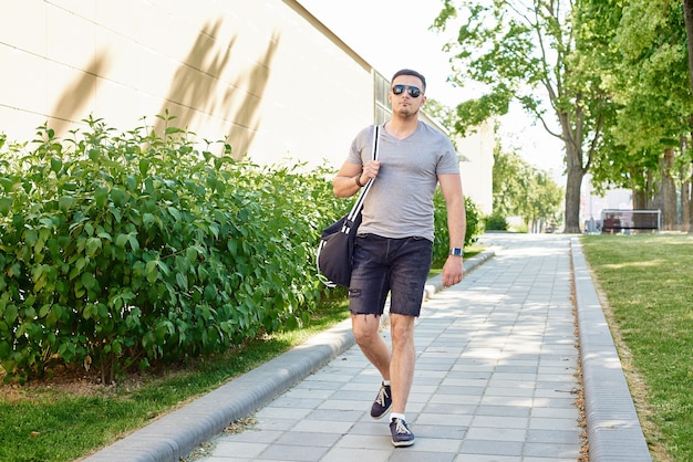 A young muscular man in sunglasses and shorts walks along the road