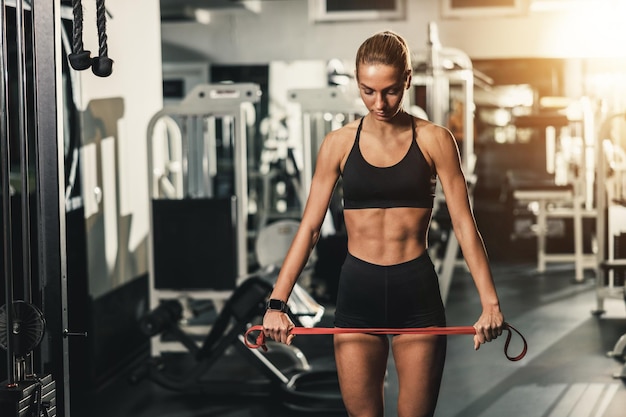 A young muscular woman doing exercises with resistance band while warming up for hard training at the gym.