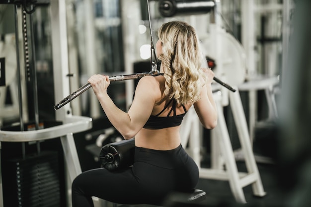 A young muscular woman is doing training on machine in the gym.