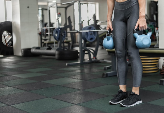 Young muscular woman in sportswear holding kettlebells in the gym. Healthy lifestyle concept. Functional training