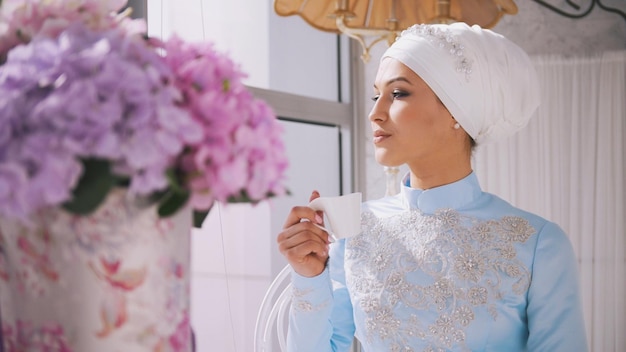 Young muslim bride in blue wedding dress drink a cup of coffee