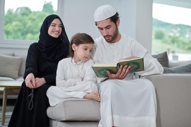 Young muslim family reading Quran during Ramadan. Parents and son worshiping to God, in islamic clothes at modern home