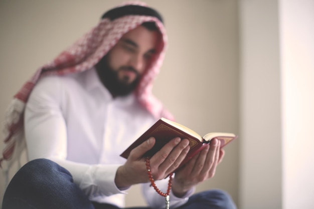 Young Muslim man reading Koran indoors