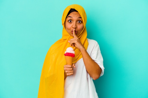 Young muslim woman eating an ice cream on blue keeping a secret or asking for silence.