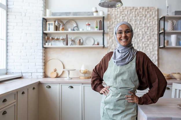 A young muslim woman food blogger trainer coach chef in hijab standing at home in kitchen at table