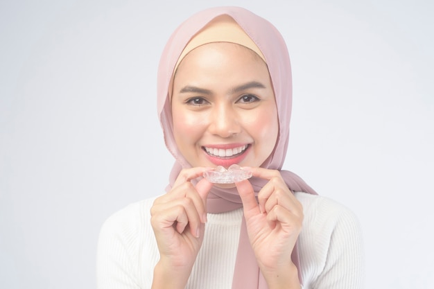 A young muslim woman holding invisalign braces on white, dental healthcare and Orthodontic concept.