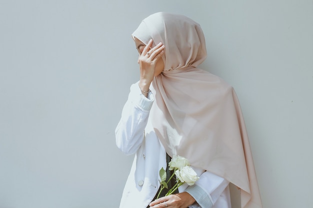 Young muslim woman holding white rose and covering her face with hand