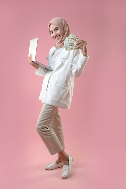 Young muslim woman working online on a laptop and holding money