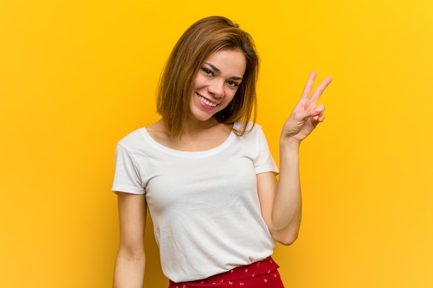 Young natural caucasian woman joyful and carefree showing a peace symbol with fingers.