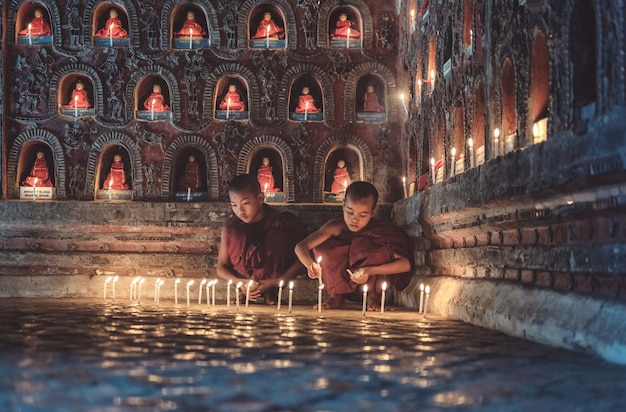 Young novice monks lighting up candlelight inside a Buddhist temple, low light setting, Shan state, Myanmar.