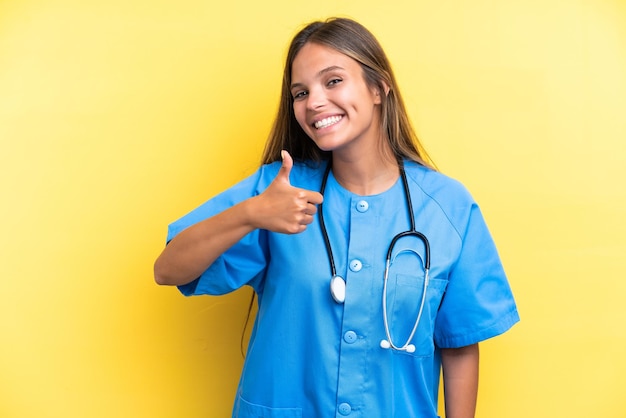 Young nurse caucasian woman isolated on yellow background giving a thumbs up gesture