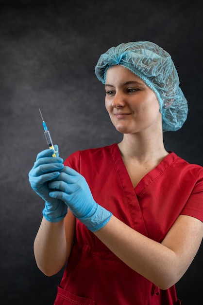 Young nurse in protective cloth holding syringe on dark background medical worker