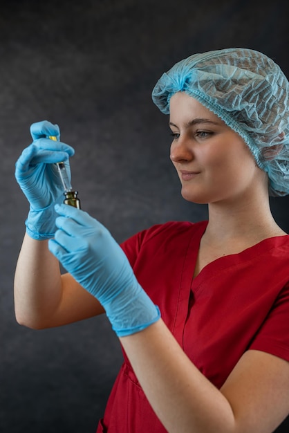 Young nurse in protective cloth holding syringe on dark background medical worker