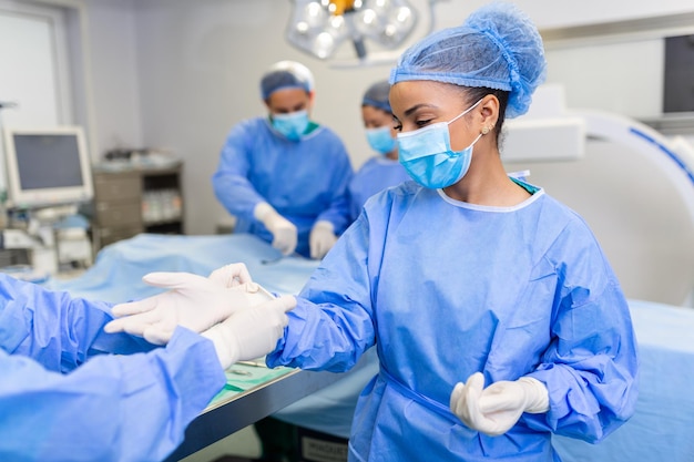 Young nurse in protective mask and workwear helping surgeon with gloves while both preparing for operation