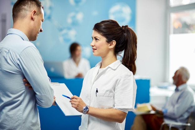 Young nurse talking to male patient about his data in medical record at the hospital