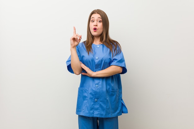 Young nurse woman against a white wall having some great idea, concept of creativity.