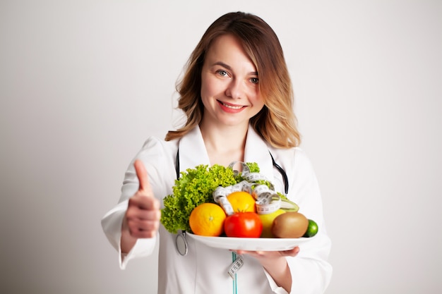 A young nutritionist holding in her hands fresh vegetables and fruits on plate in the consultation room