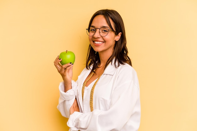 Young nutritionist woman holding a weighing machine isolated on yellow background