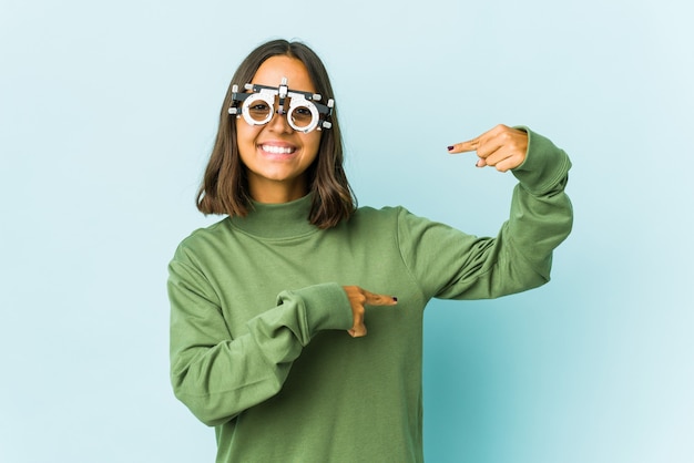 Young oculist latin woman holding something little with forefingers, smiling and confident.