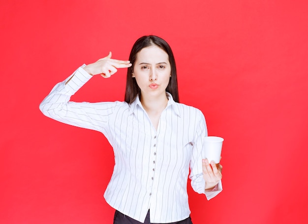 Young office employee standing with plastic cup of tea over red wall. 