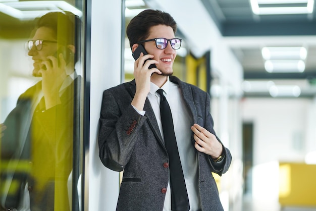 Young office worker in glasses using mobile smart phone Businessman holds telephone in hand