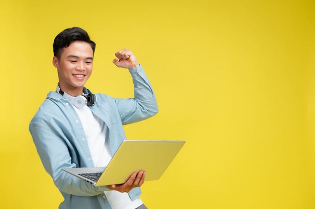 Young overjoyed man walking going hold use work on laptop do winner's gesture clenched fist isolated